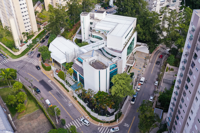 Vista aérea do Colégio Porto Seguro no Morumbi, com arquitetura interligada por passarelas. O local está cercado por árvores e ruas com carros estacionados, em um ambiente urbano.