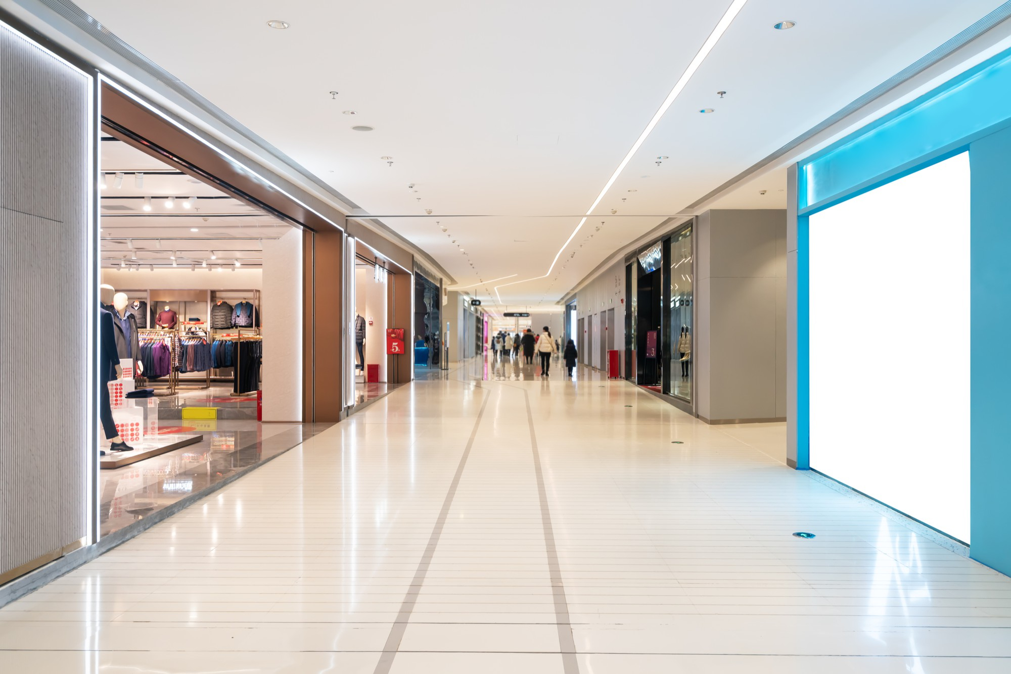 Corredor de shopping center moderno e iluminado, com vitrines de lojas à mostra e algumas pessoas caminhando ao fundo.