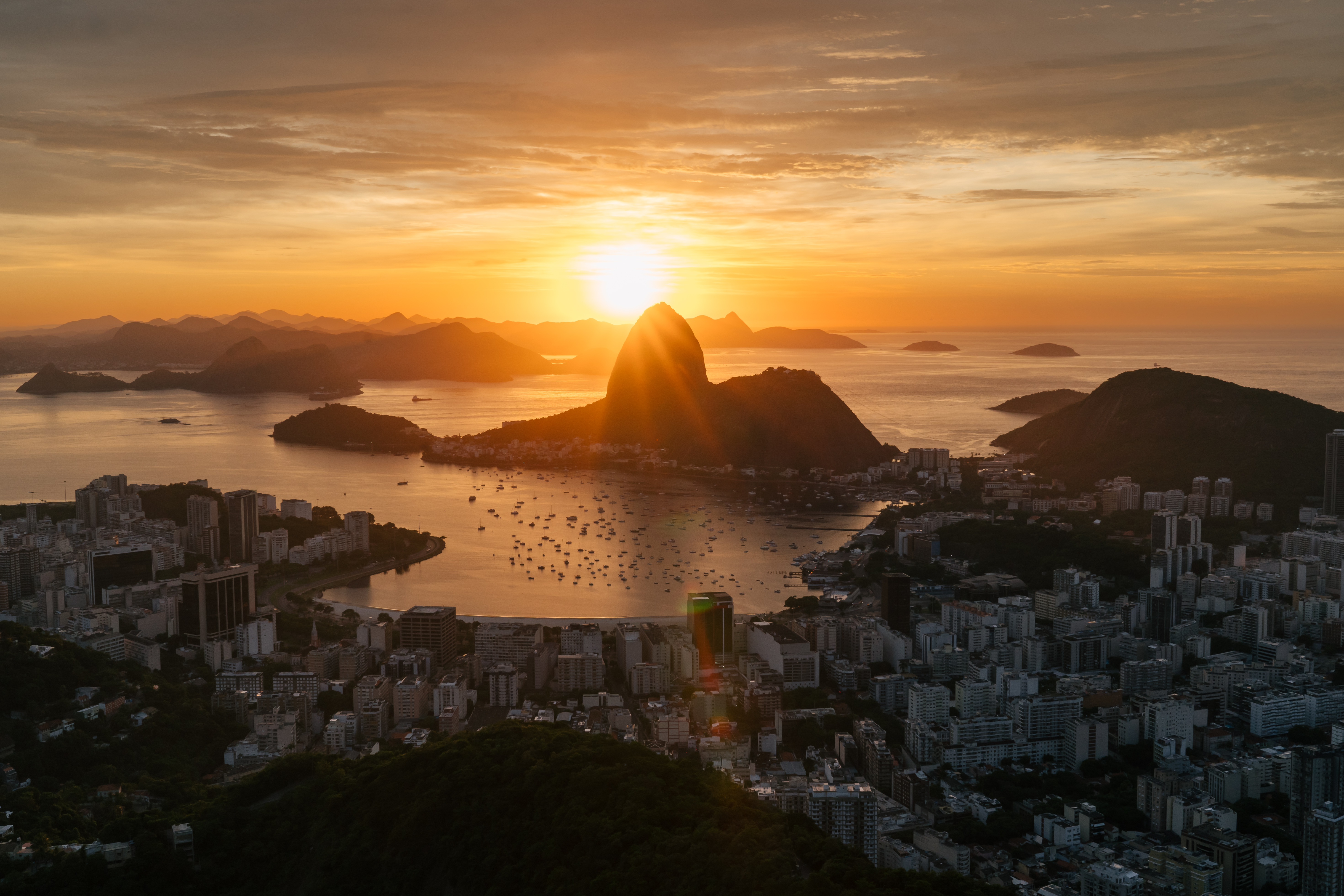 Nascer do sol no Rio de Janeiro: Pão de Açúcar em silhueta, baía dourada com barcos e a cidade despertando.