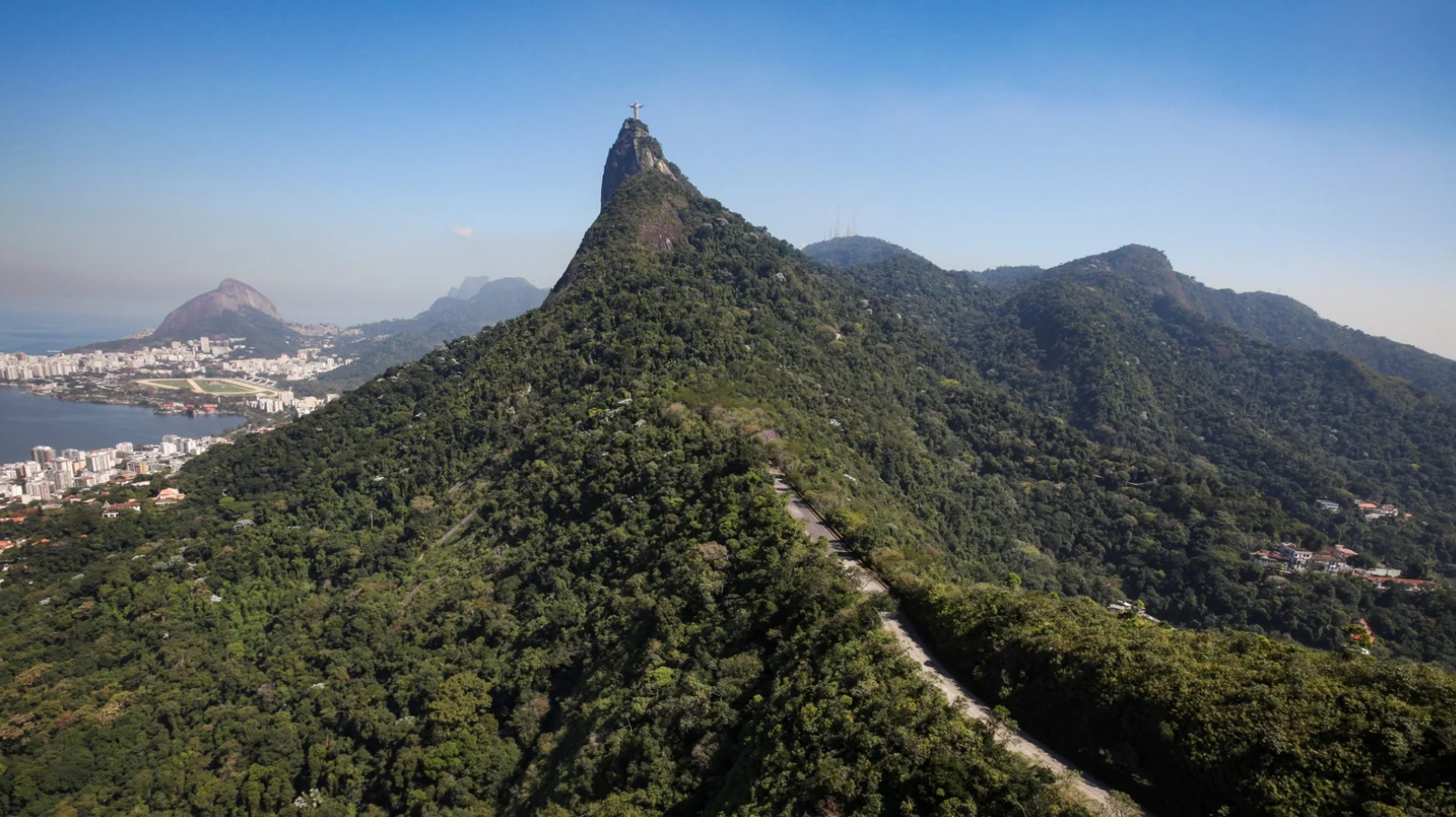 Vista aérea do Parque Nacional da Tijuca, Rio de Janeiro, com o Cristo Redentor no Corcovado. Floresta densa e verde domina a paisagem, com a cidade e a Lagoa Rodrigo de Freitas visíveis ao fundo.