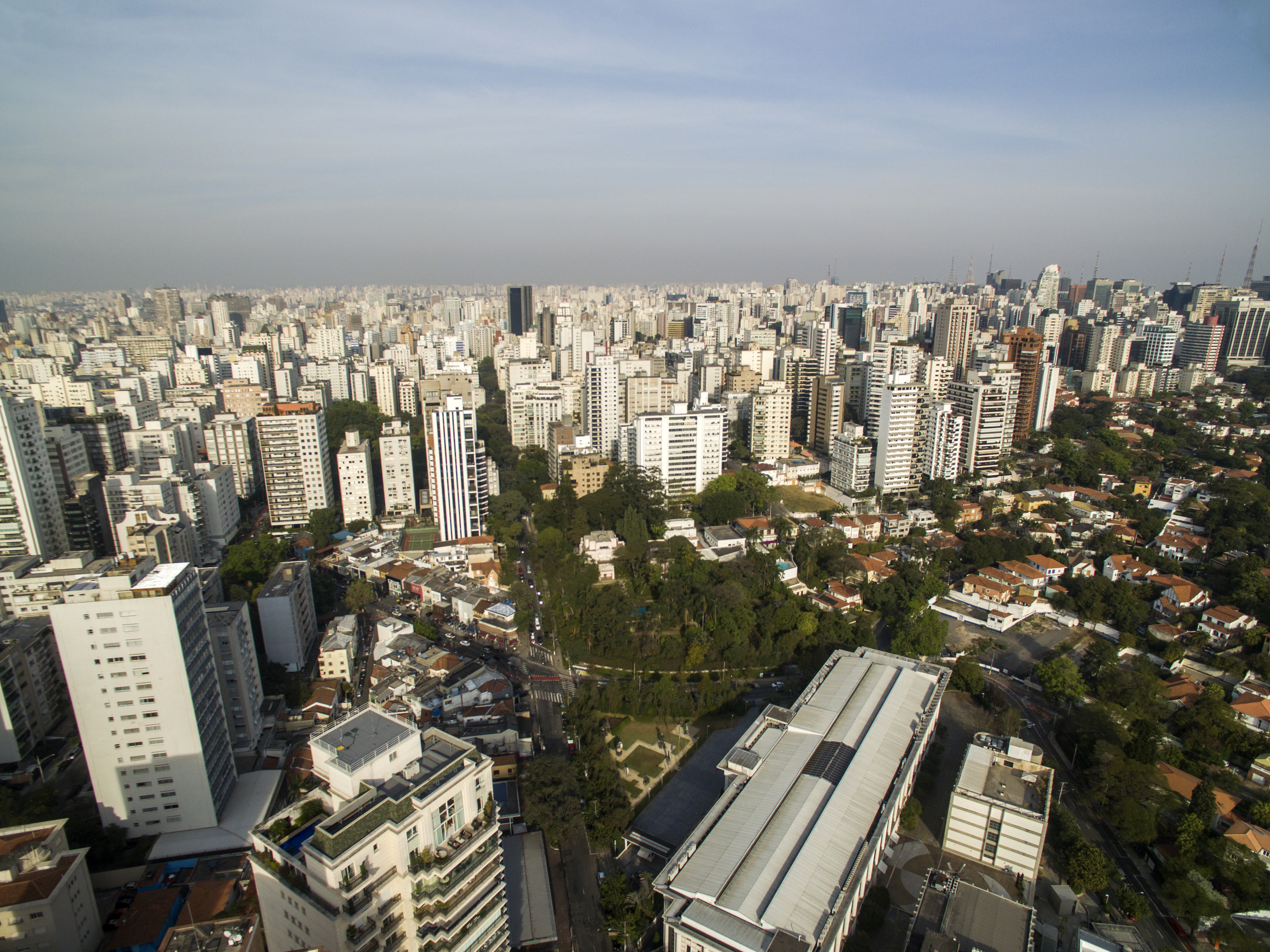 Vista aérea panorâmica da cidade de São Paulo, mostrando uma vasta extensão de edifícios altos e densamente construídos sob um céu claro.