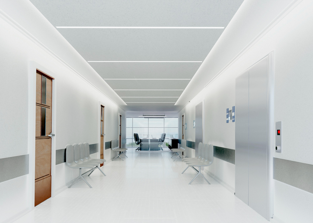 Um corredor de hospital ou clínica branco e limpo com fileiras de cadeiras de espera cinzas, portas de madeira, elevadores e uma área de recepção ao fundo.