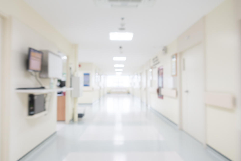 Um corredor de hospital longo e bem iluminado, desfocado, com paredes claras e equipamentos médicos nas laterais.