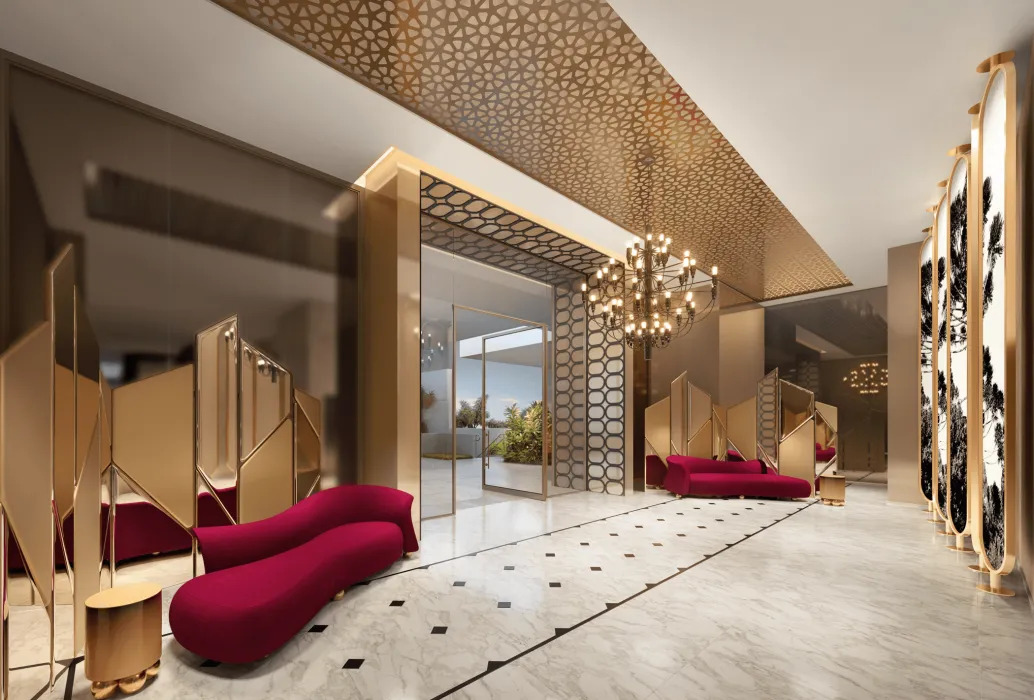 Lobby luxuoso com teto dourado e padrões geométricos, piso de mármore, sofás curvos vermelhos, espelhos decorativos e um grande lustre, levando a uma área externa.